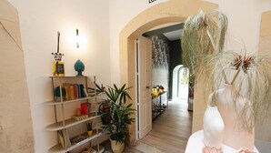 Un rincón acogedor para leer con una estantería, una planta en maceta y un jarrón con plantas secas.