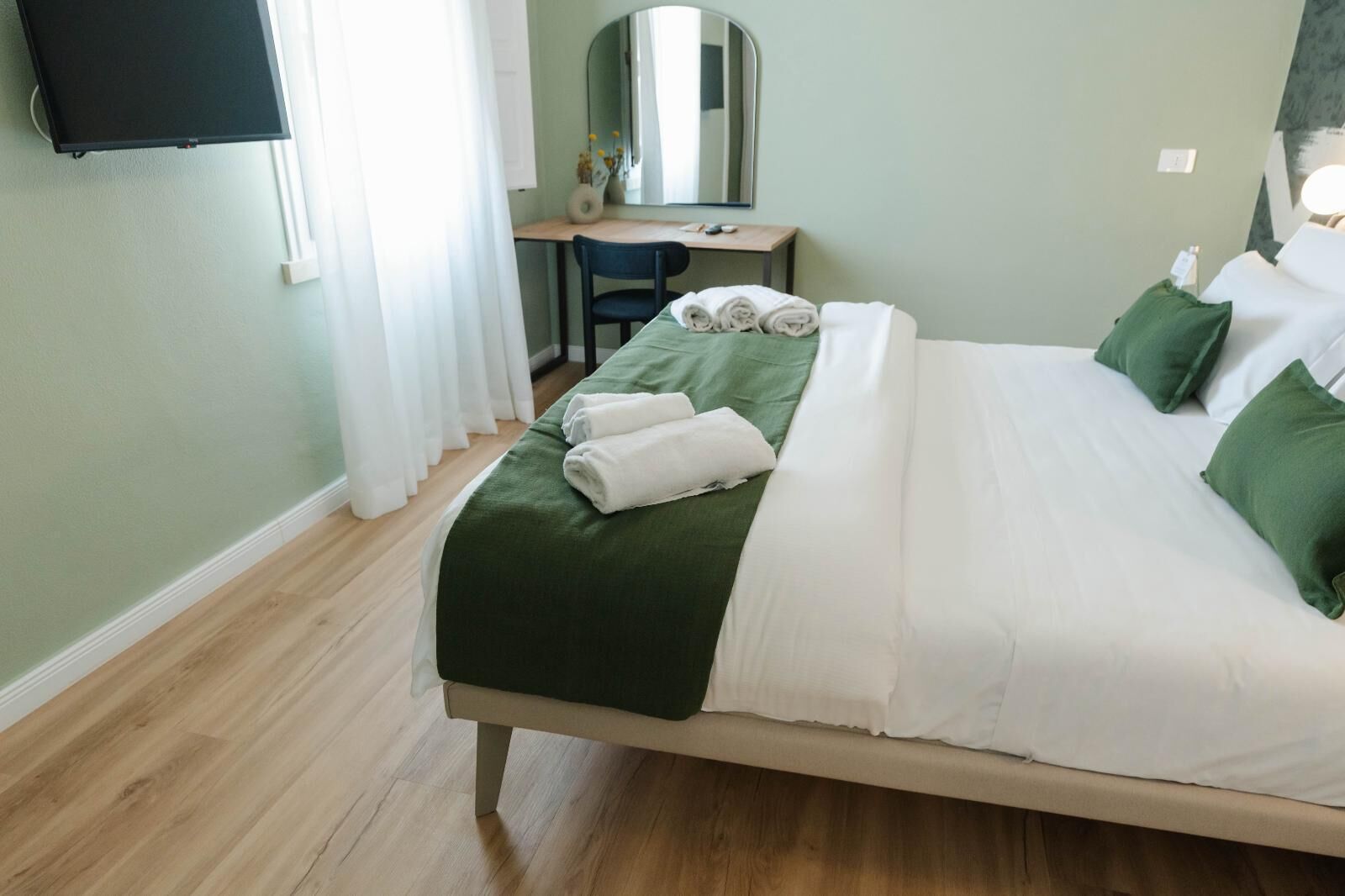 Ein Hotelzimmer mit einem Bett, einem Schreibtisch, einem Sessel, einem Spiegel und einem Fernseher an der Wand.