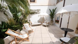 Un patio soleado con sillones de descanso, una pequeña mesa y sombrillas.