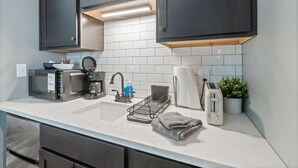 A modern kitchen with a microwave, coffee maker, sink, and toaster. - Hearthstone Hideaway at Tudor Suites (Eureka Springs)