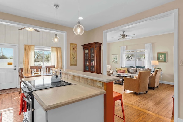 A kitchen with an island, dining area with chairs, a living room with a sofa, and a ceiling fan.