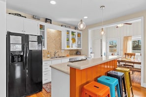 A modern kitchen with a black refrigerator, white cabinets, a wooden island, and colorful stools.