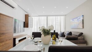 A modern dining area with a white table set for two, a vase with white flowers, and a bottle of wine. There is a sofa and a painting on the wall. - Enjoy easy access to Sliema Seafront and Tigne Point just on your doorstep (Tas-Sliema)