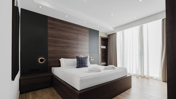 A modern hotel room with a large bed, dark wood paneling, and a large window with curtains. - Enjoy easy access to Sliema Seafront and Tigne Point just on your doorstep (Tas-Sliema)