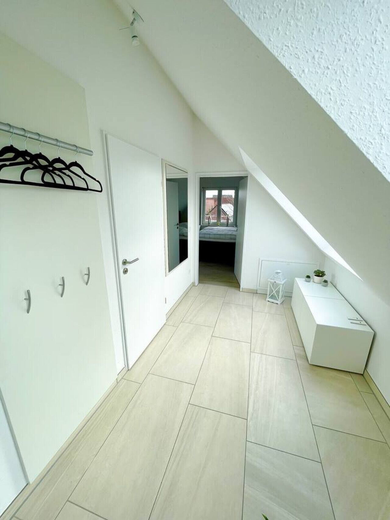 A narrow hallway with a sloped ceiling, a white door, and a small window.