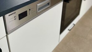 A modern kitchen with a built-in dishwasher and oven, a window above the sink, and a countertop.