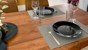 A dining table set with plates, cutlery, and glasses, with a modern kitchen in the background.