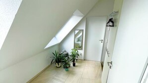 A narrow, sloped hallway with tiled flooring, a white door, and a small window.