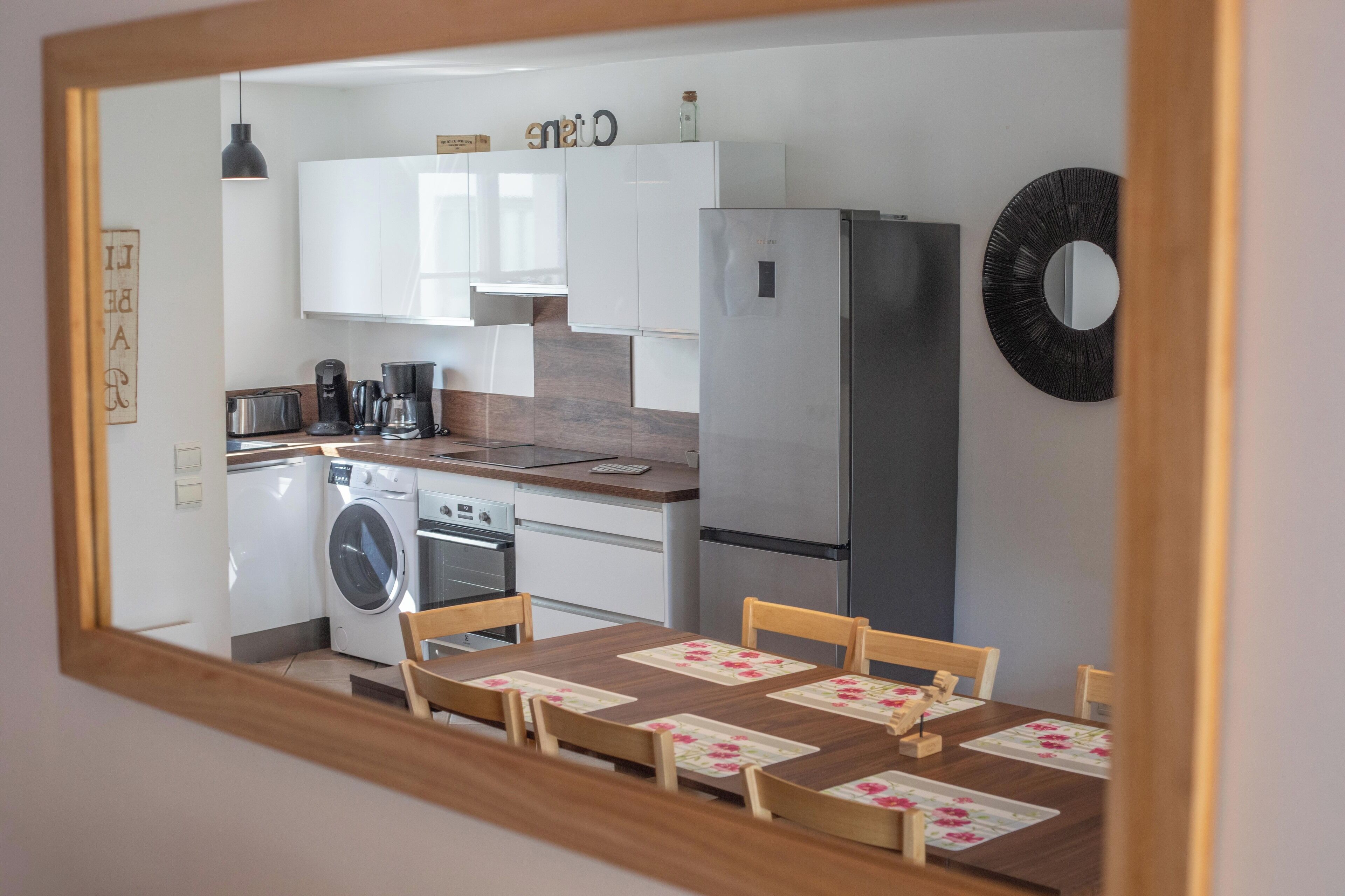 A compact kitchen with a washing machine, a refrigerator, and a dining area with a table and chairs.