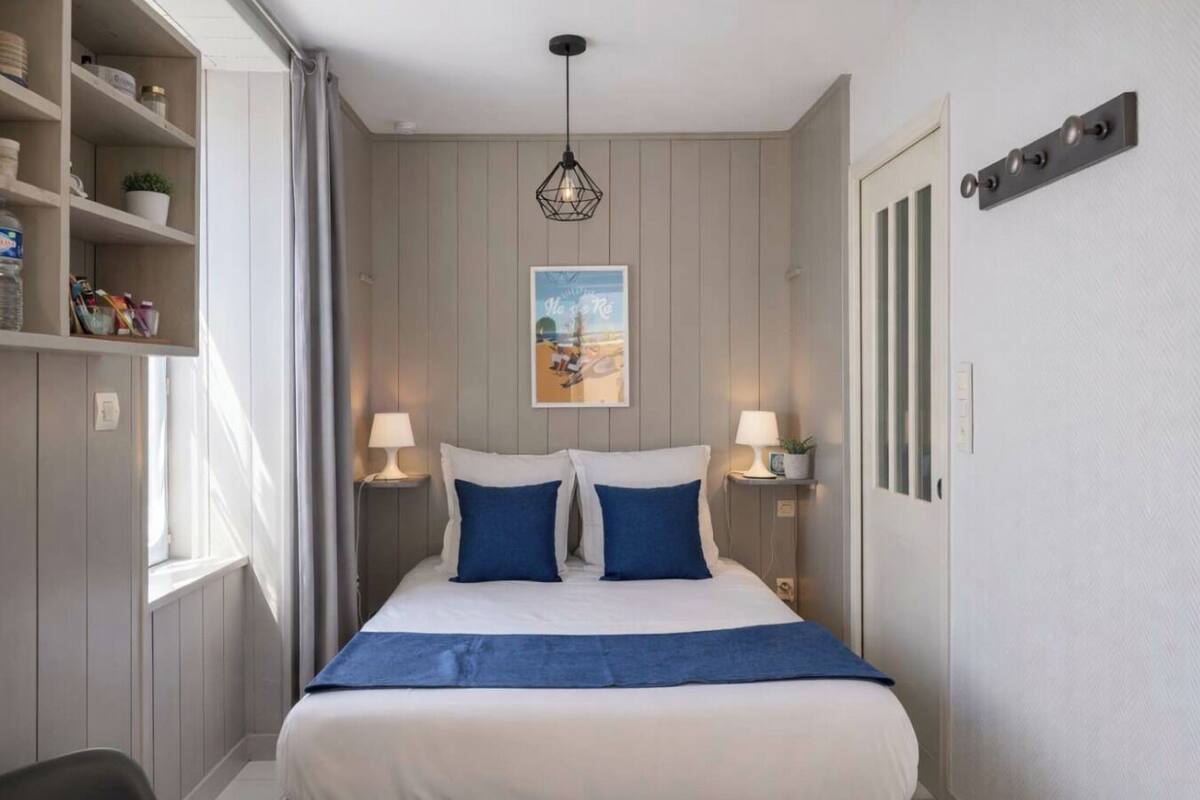 Ein Schlafzimmer mit einem Bett, zwei Nachttischlampen, einem Wandbild und einem Regal mit Gegenständen.