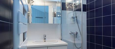 A modern bathroom with a glass shower enclosure, a white sink, and a blue-tiled wall.