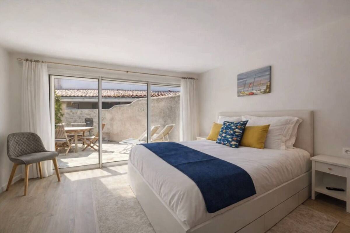 Ein Schlafzimmer mit einem großen Bett, einem Sessel, einem kleinen Tisch und Blick ins Freie.