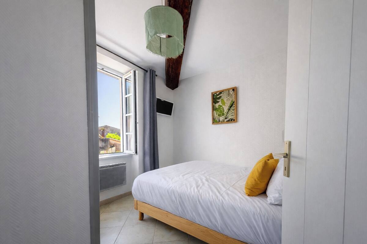 Ein Schlafzimmer mit Bett, Fenster, Fernseher und einer Pflanze.