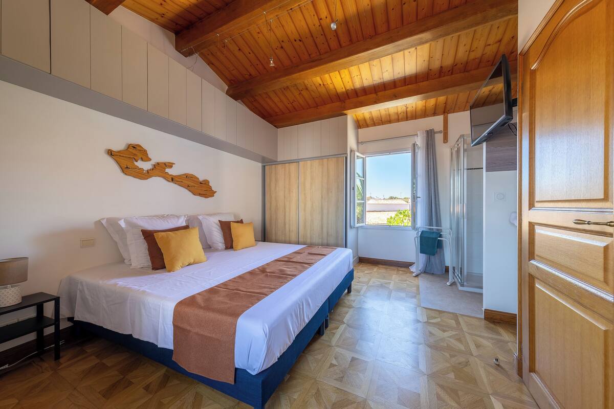Ein Schlafzimmer mit Bett, Holzboden und Blick durch eine Tür.