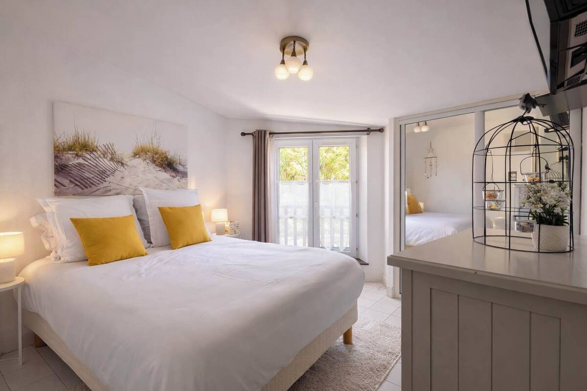Ein Schlafzimmer mit Bett, Nachttischen, einem Spiegel, einem Vogelkäfig und einem Fenster mit Vorhängen.