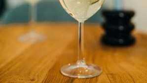 Ein Glas Weißwein auf einem Holztisch, im Hintergrund brennt eine Kerze.