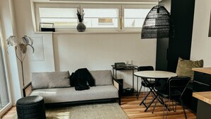 A modern living room with a grey sofa, a round dining table with black chairs, a black ottoman, and a small side table. - Industrial Loft | Smart TV | High-Speed WiFi (Düsseldorf)