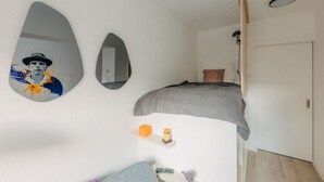 A bedroom with a bed, a mirror, a shelf with a bottle, and a door.