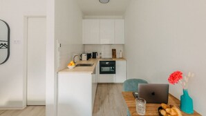 A modern kitchen with white cabinets, a sink, and a countertop. There is a laptop, a vase with flowers, and a bowl of fruit on the counter. - Central Stay | Design Apartment | Balcony & WiFi (Düsseldorf)