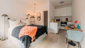 A modern bedroom with a bed, bedside table, and a small kitchenette area. - Central Stay | Design Apartment | Balcony & WiFi (Düsseldorf)