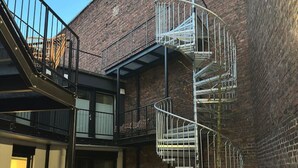 A spiral staircase with metal railings, a brick building, and a door with a shutter. - Boho Meets Modern - The Perfect City Escape (Düsseldorf)
