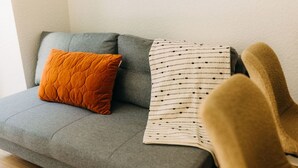 A grey sofa with a quilted orange pillow and a striped blanket. - Boho Meets Modern - The Perfect City Escape (Düsseldorf)