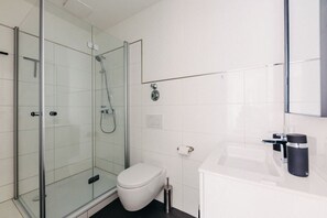 Ein modernes Badezimmer mit einer Duschkabine aus Glas, einer weißen Toilette und einem weißen Waschbecken mit schwarzem Wasserhahn.