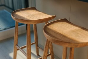 Zwei hölzerne Hocker mit gebogenen Sitzen und Metallbeinen, neben einer Wand platziert.