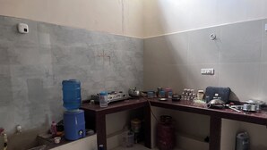 A kitchen with a marble backsplash, a water dispenser, a gas cylinder, and various kitchen utensils. - R K Lodge And Palace  (Ayodhya)