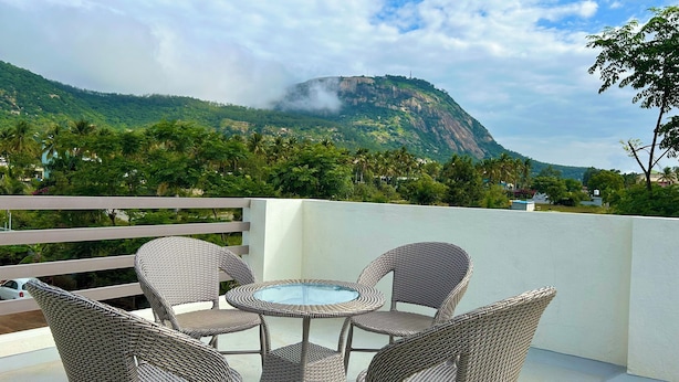 Ein Balkon mit Korbmöbeln und einem Glastisch, mit Blick auf eine gebirgige Landschaft mit viel Grün und einigen Gebäuden.