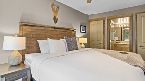 A neatly made bed with a wooden headboard, two bedside lamps, and a decorative deer head on the wall.