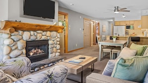 A living room with a stone fireplace, a flat-screen TV, a ceiling fan, and a dining area with a table and chairs.