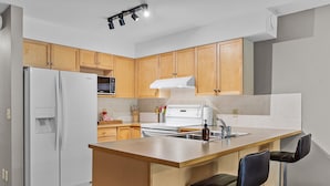 A modern kitchen with wooden cabinets, a white refrigerator, a stove, and a bar area with two stools.