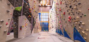 An indoor climbing gym with multiple climbing walls, padded flooring, and a large window at the end. - Creekside Condo | Main Street | Mountain Views (Canmore)