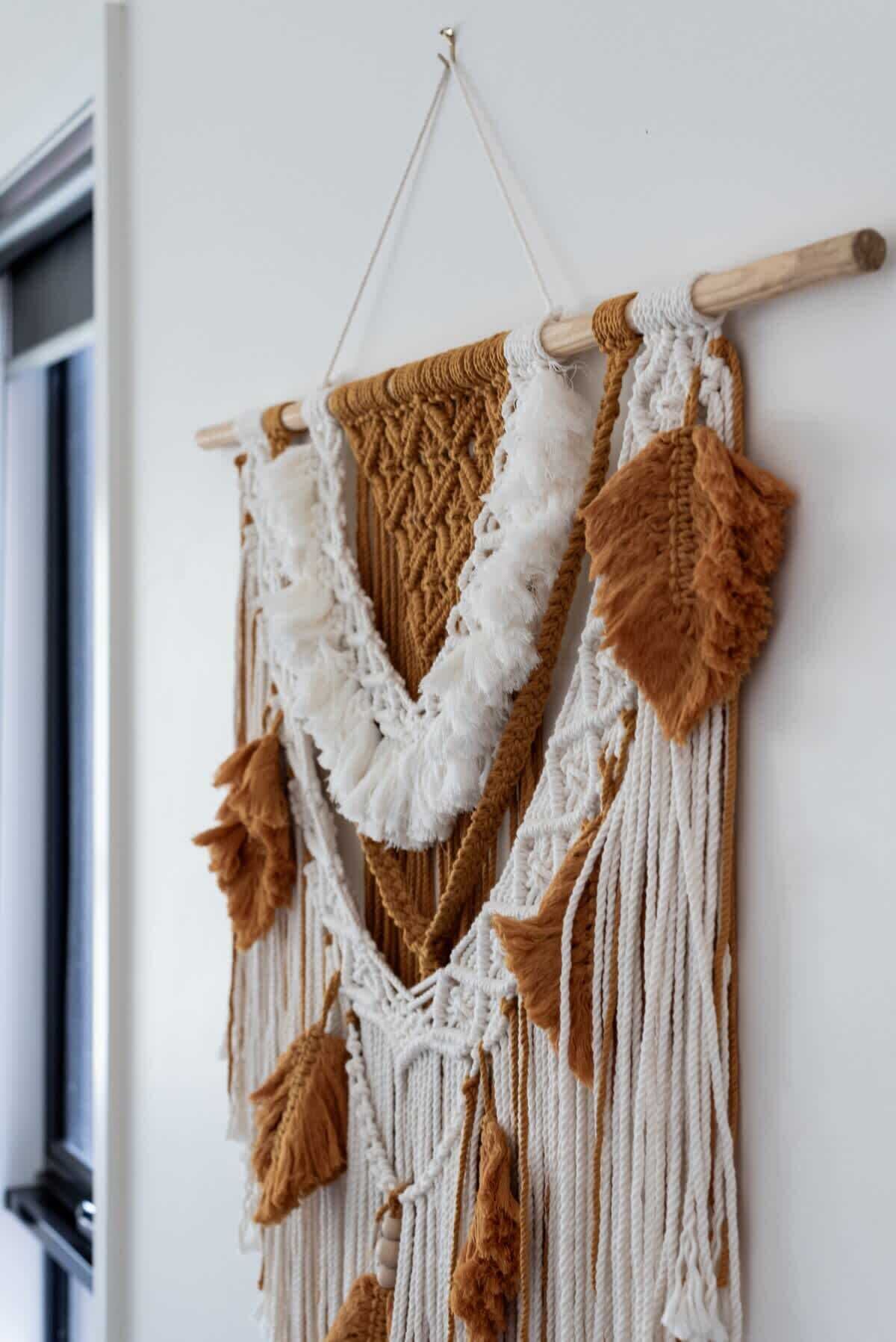 A macrame wall hanging with a wooden hanger.