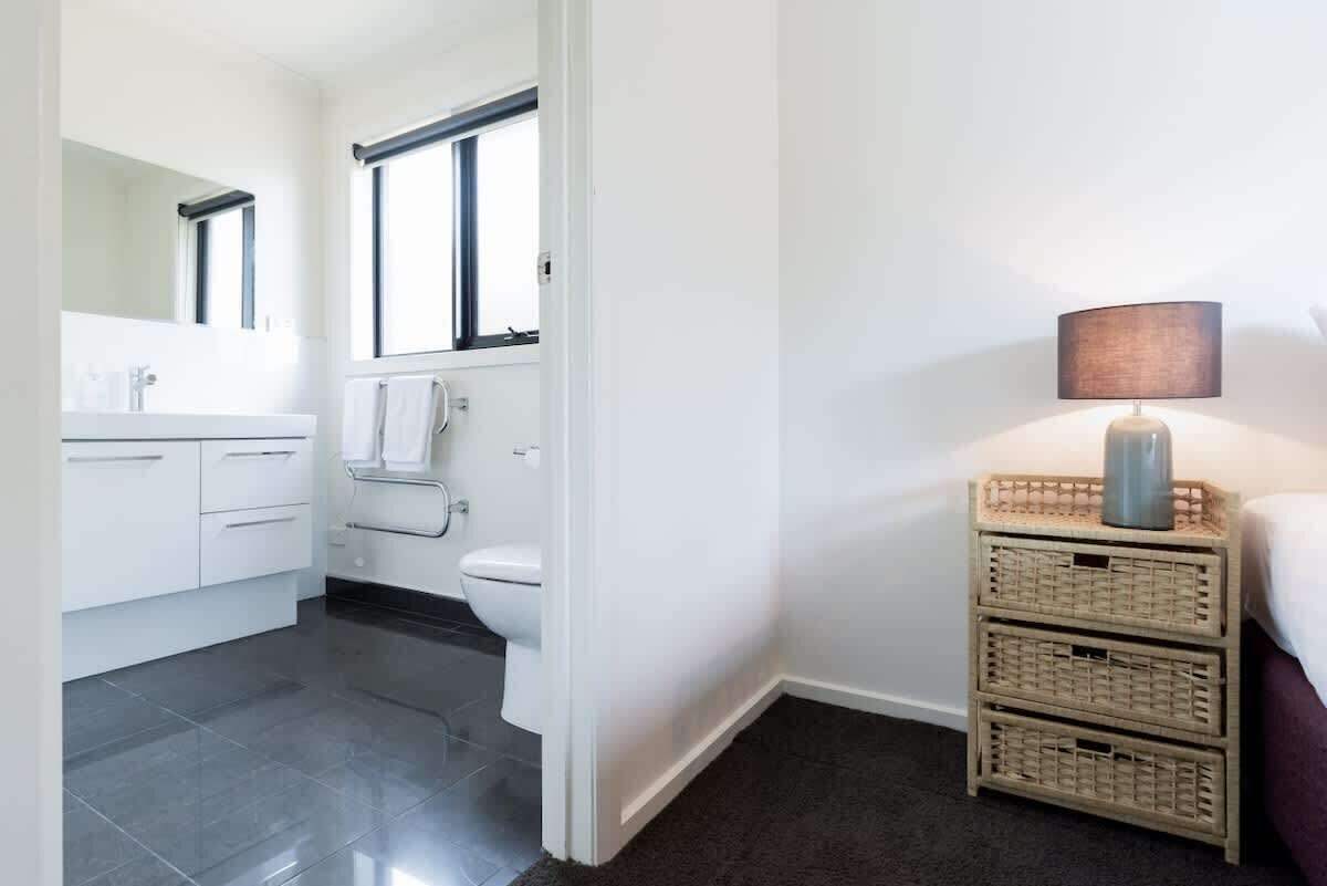 A bathroom with a toilet, sink, and mirror, a dark floor, and wicker baskets.