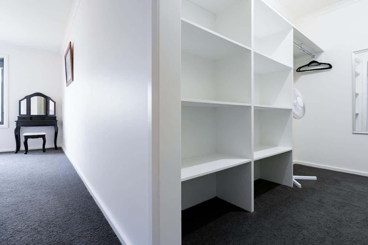 A room with a white wall, a black piano, and a white shelving unit with a hanging garment.