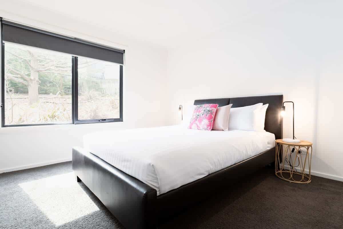 A bedroom with a large window, a bed with white bedding, and a bedside lamp.