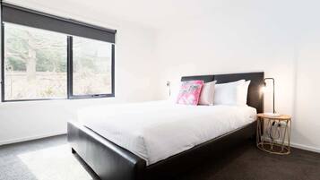 A bedroom with a large window, a bed with white bedding, and a bedside lamp.