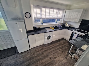 Cocina compacta con muebles blancos, lavadora integrada, estufa y lavabo.