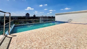 Une piscine sur le toit, avec une eau d’un bleu cristallin, une terrasse carrelée et une vue sur le paysage urbain en arrière-plan.
