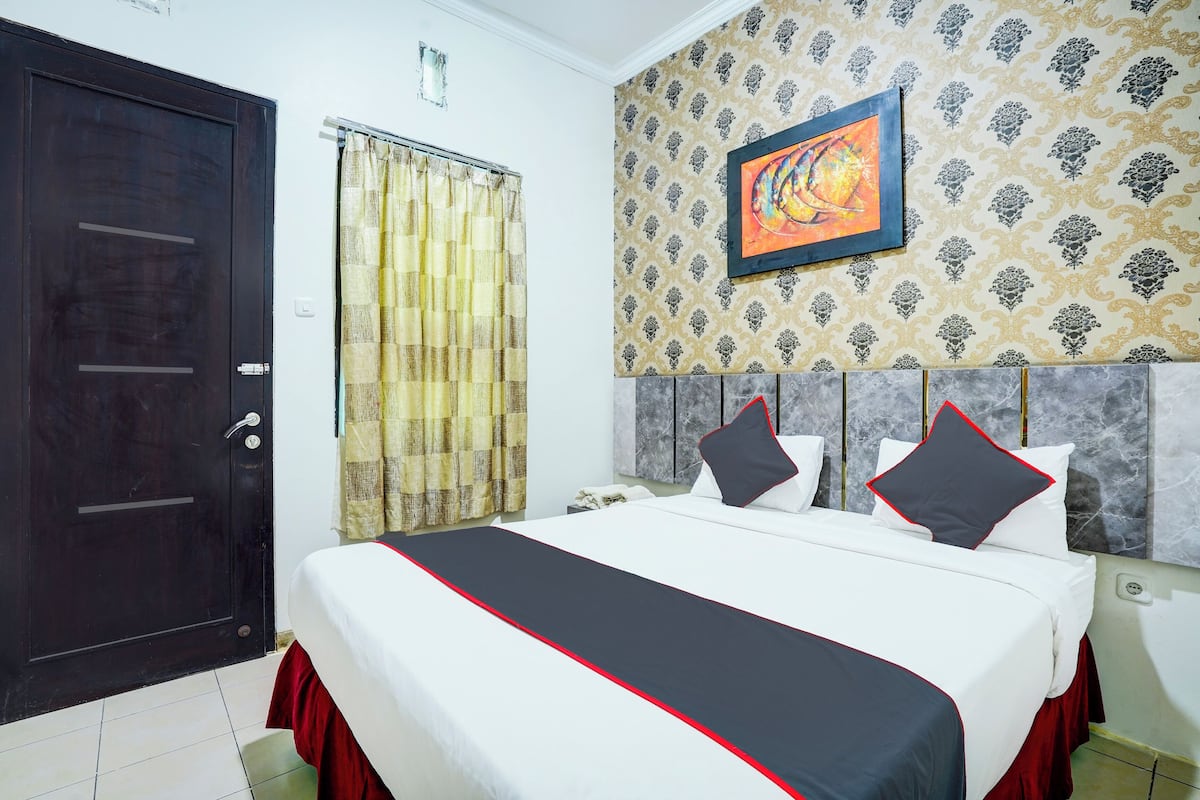 A hotel room with a large bed, a dark door, a patterned wallpaper, and a framed artwork on the wall.
