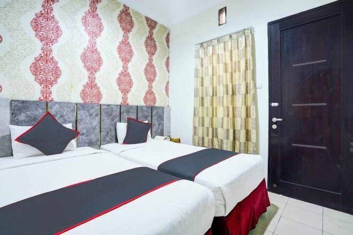 A hotel room with two beds, a patterned wall, a curtain, and a dark door.