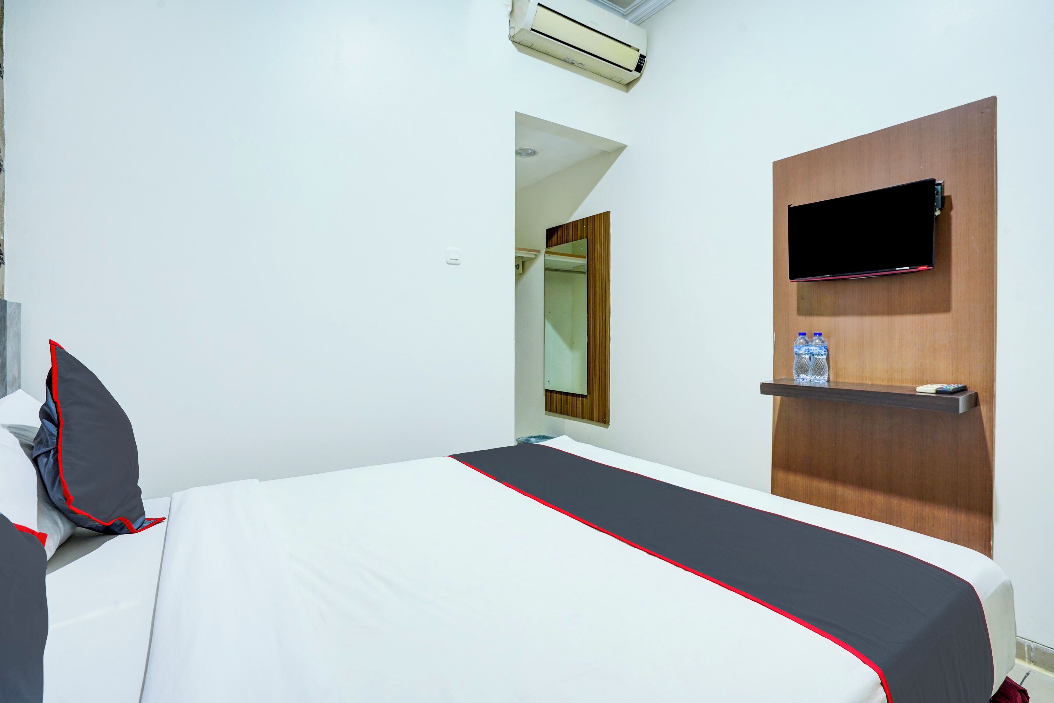 A hotel room with a bed, a TV mounted on the wall, and a shelf with a water bottle.