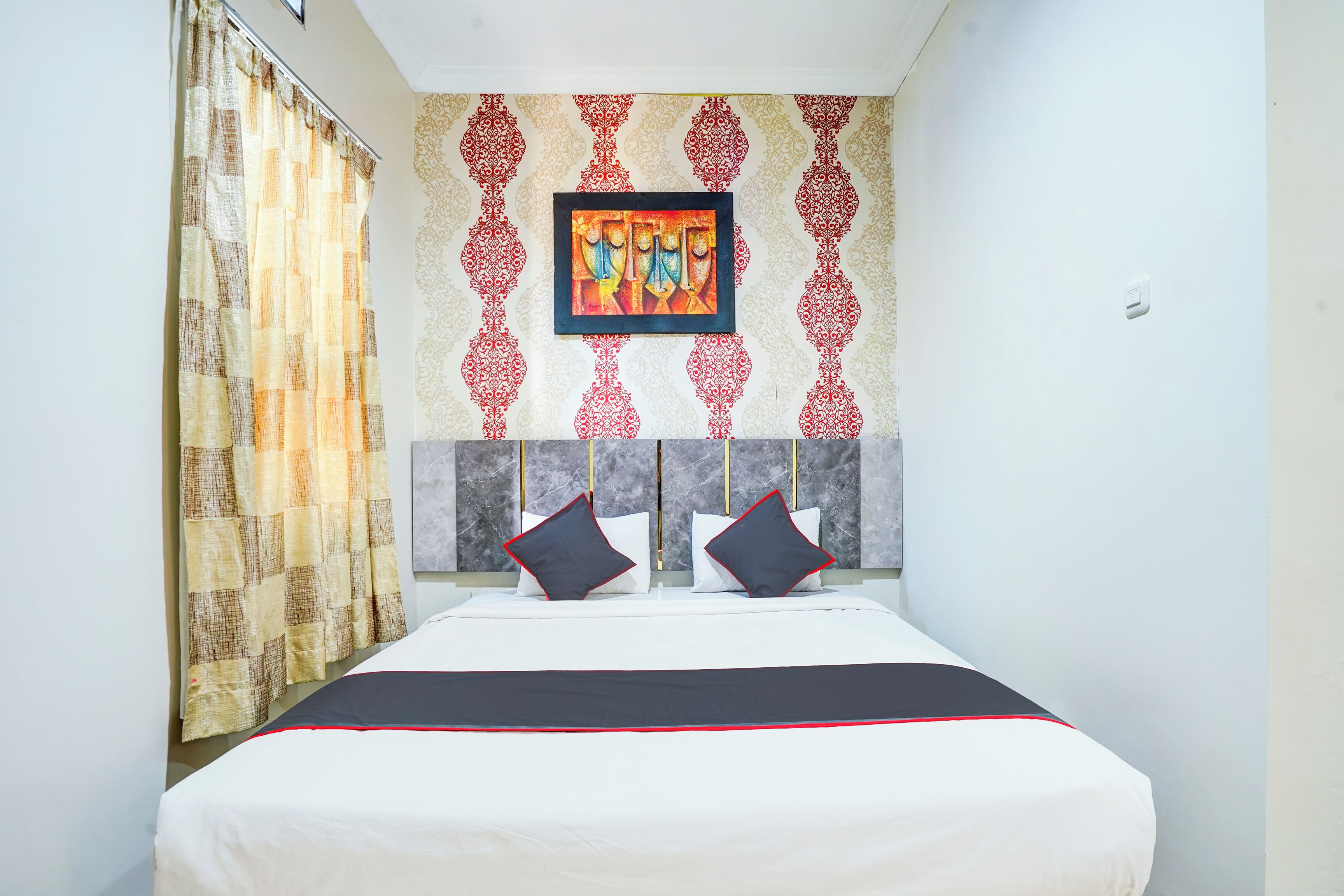 Una habitación de hotel con cama, cortina estampada, una obra de arte enmarcada en la pared y cabecera de mármol.