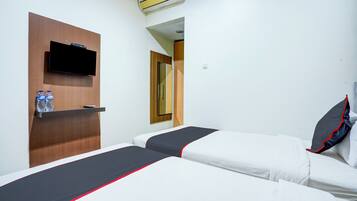 A hotel room with two beds, a mounted TV, and a shelf with water bottles.