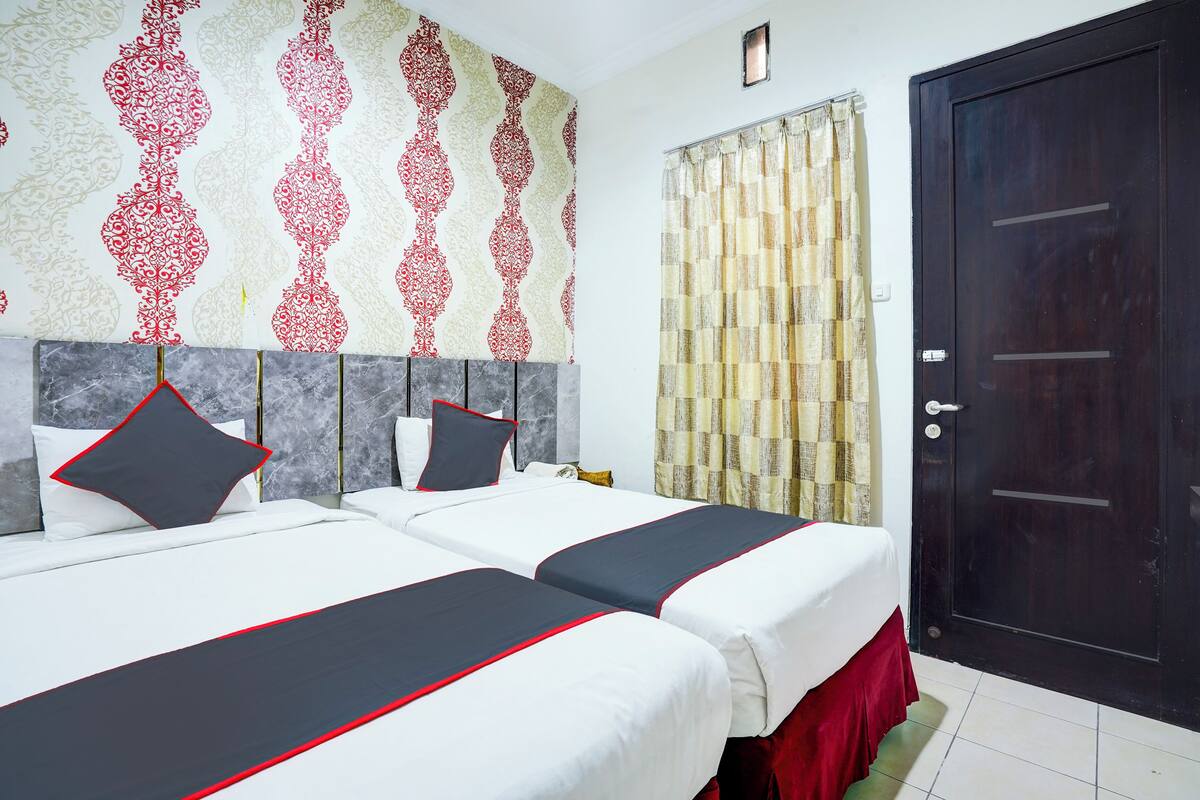 A hotel room with two beds, a dark wooden door, patterned wallpaper, and a curtain.
