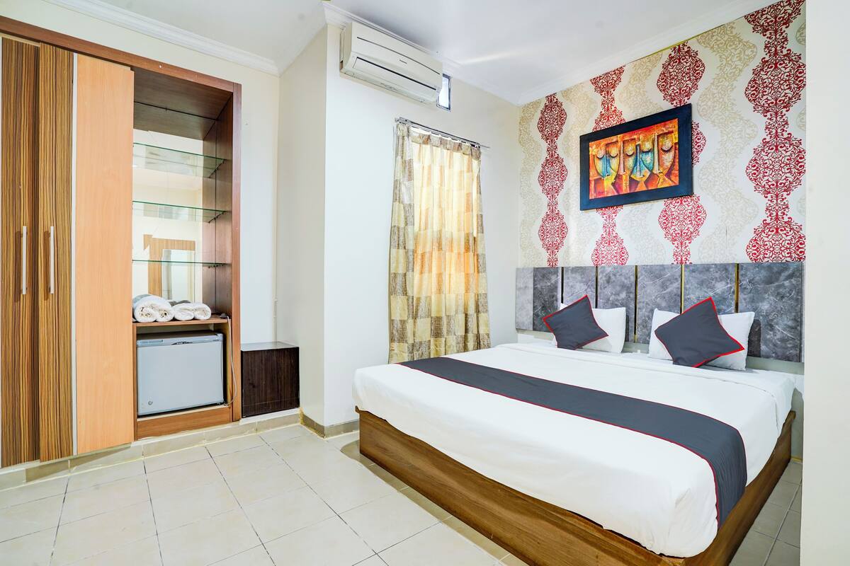A hotel room with a bed, a wardrobe, a small fridge, and a shower curtain.