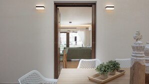 A room with a wooden table, white chairs, a tray with potted plants, and a view of a balcony with a green sofa.