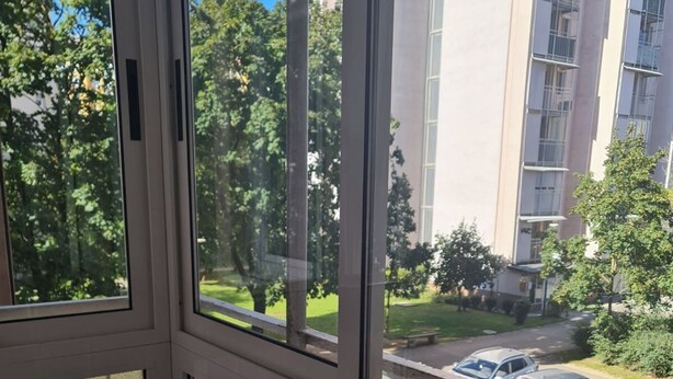 A view from a window with frosted glass panels, overlooking a parking area with cars and a building with multiple floors and balconies. - Studio Beni (Ljubljana)